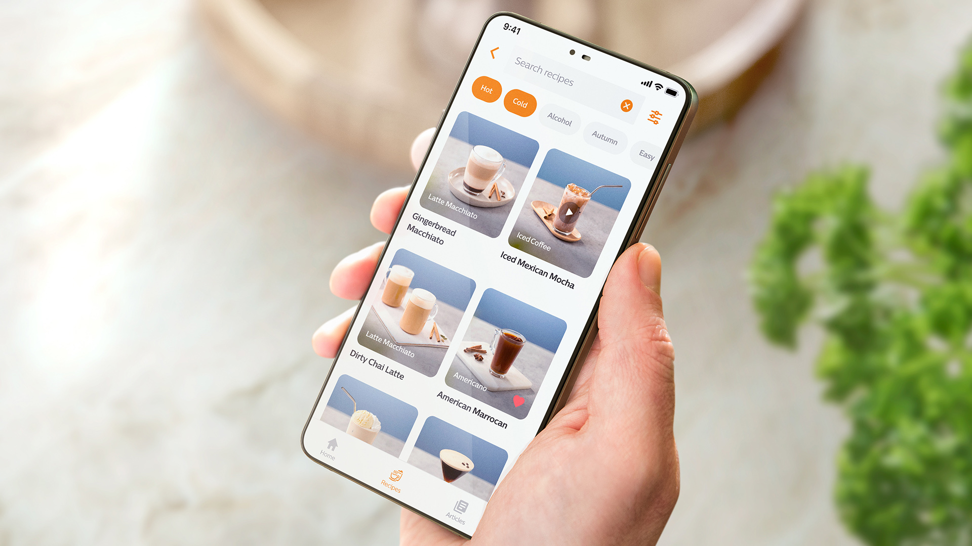 En person som holder en smarttelefon som viser HomeID-appen med kaffedrikkealternativer. En person som holder en smarttelefon som viser HomeID-appen med kaffedrikkealternativer.