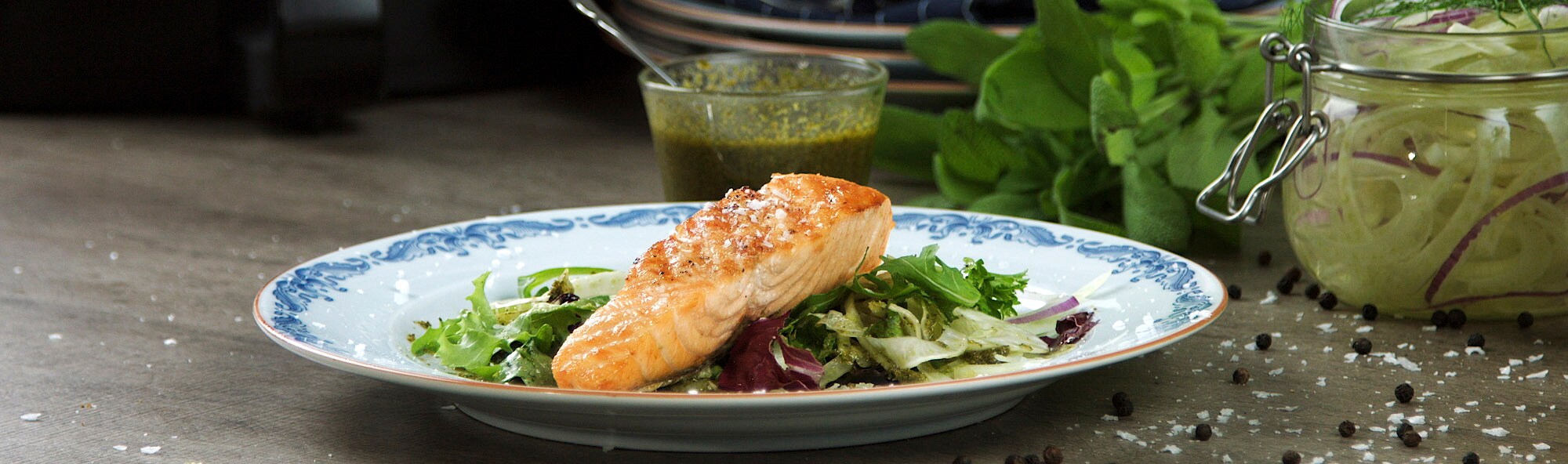 Lax med sallad på en blåvit tallrik. I närheten av grön sås, salvia och picklad lök Lax med sallad på en blåvit tallrik. I närheten av grön sås, salvia och picklad lök