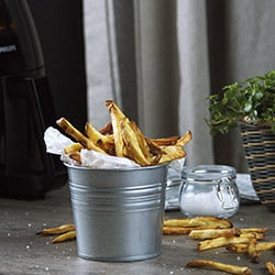 Air-fried potatoes inside a silver bucket, some potatoes have fallen onto a plate. Air-fried potatoes inside a silver bucket, some potatoes have fallen onto a plate.
