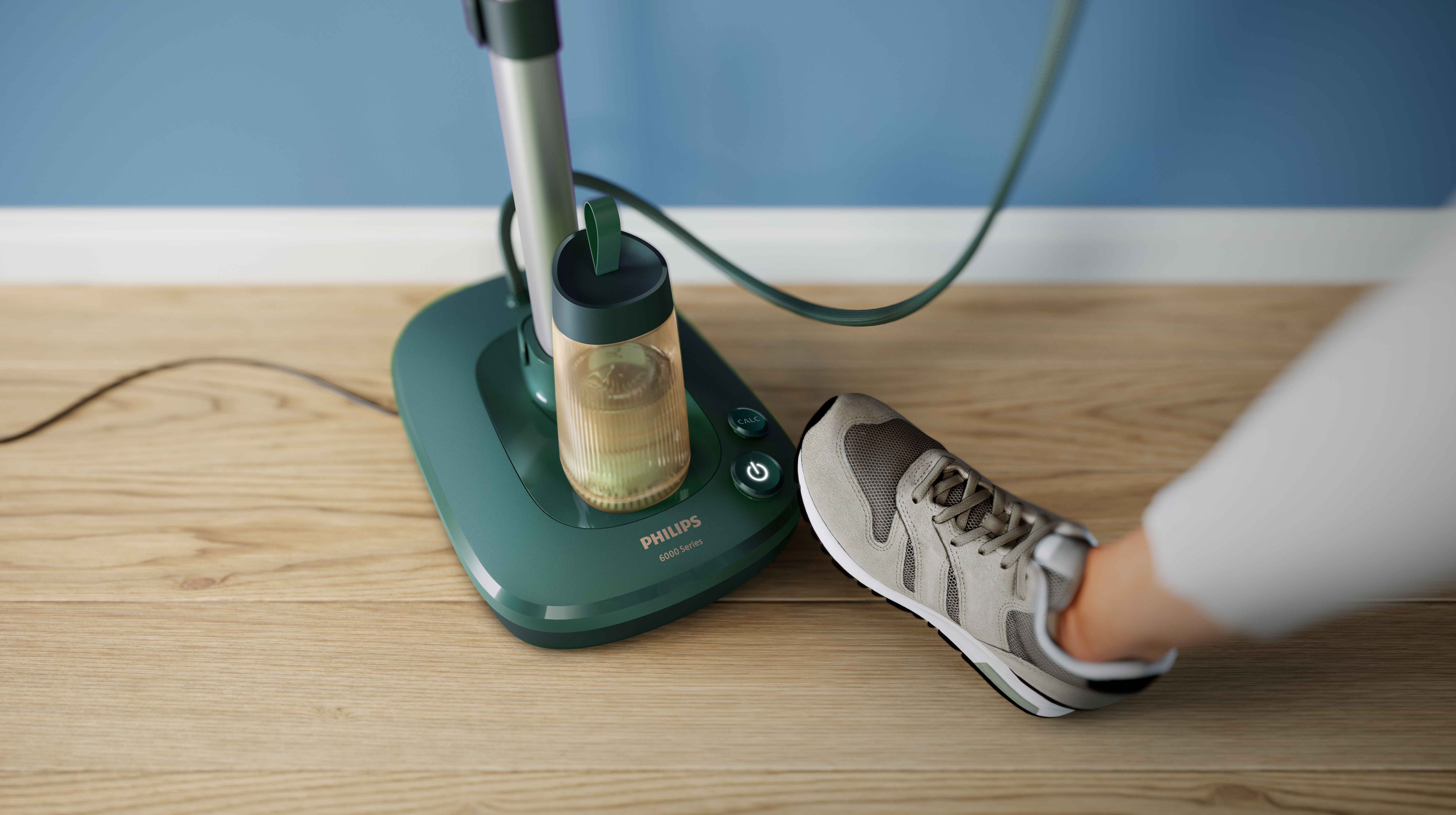 Nærbilde av Philips All-in-One Garment Care steamer på tregulv, en sko som referanse. Viser kompakt design, fylt vanntank, strømknapp og kalkrenseknapp for optimal bruk. Nærbilde av Philips All-in-One Garment Care steamer på tregulv, en sko som referanse. Viser kompakt design, fylt vanntank, strømknapp og kalkrenseknapp for optimal bruk.