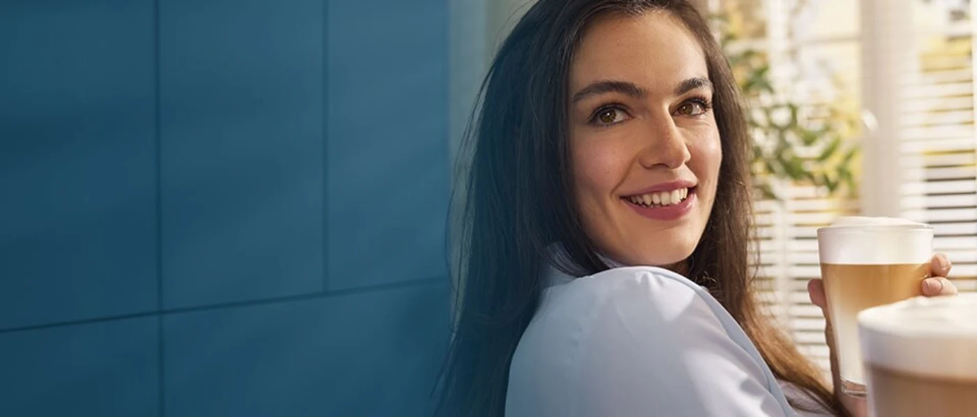 Eine Frau hält eine Kaffeetasse vor sich und lächelt. Eine Frau hält eine Kaffeetasse vor sich und lächelt.