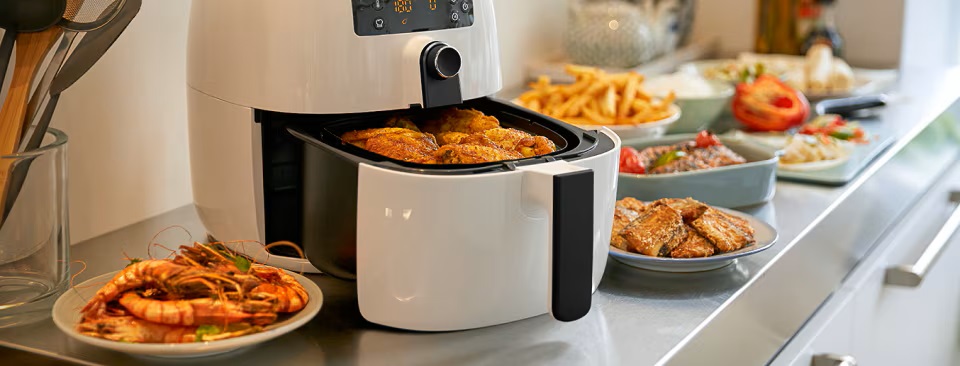 Biała frytkownica Philips z różnorodnymi potrawami wyeksponowanymi na blacie kuchennym. Biała frytkownica Philips z różnorodnymi potrawami wyeksponowanymi na blacie kuchennym.