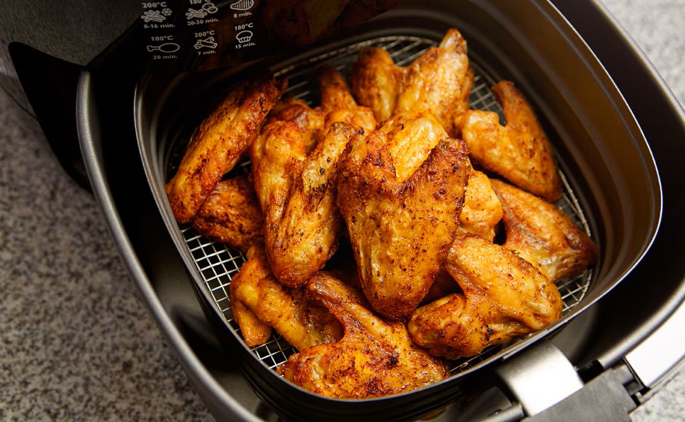 Zbliżenie na kosz airfryera zawierający chrupiące skrzydełka z kurczaka w frytkownicy, gotowe do przyrządzenia. Zbliżenie na kosz airfryera zawierający chrupiące skrzydełka z kurczaka w frytkownicy, gotowe do przyrządzenia.