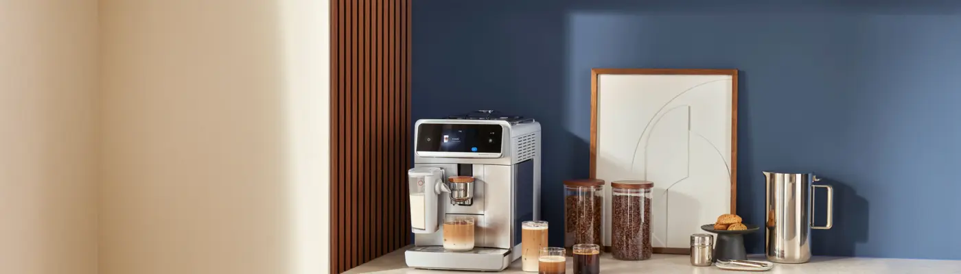 A Philips automatic espresso machine on a kitchen counter with several cups of coffee drinks, jars of beans, and a pitcher beside it. A Philips automatic espresso machine on a kitchen counter with several cups of coffee drinks, jars of beans, and a pitcher beside it.