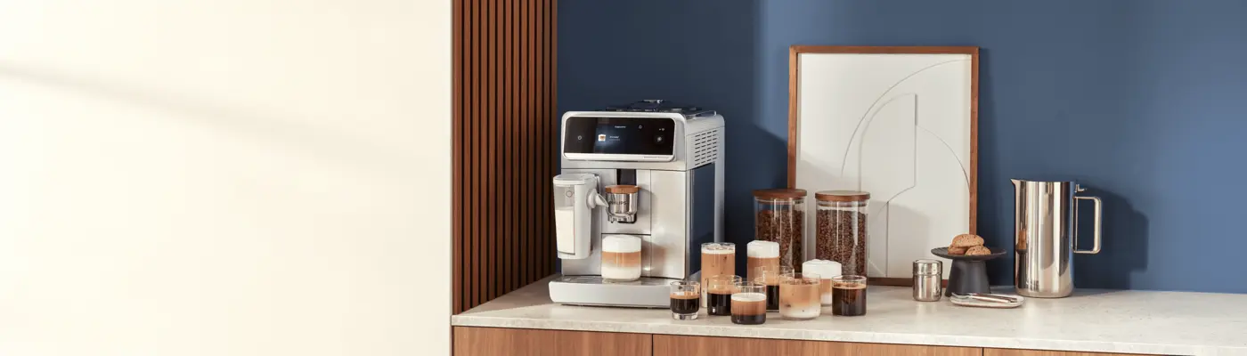 A Philips automatic espresso machine on a kitchen counter with several cups of coffee drinks, jars of beans, and a pitcher beside it. A Philips automatic espresso machine on a kitchen counter with several cups of coffee drinks, jars of beans, and a pitcher beside it.