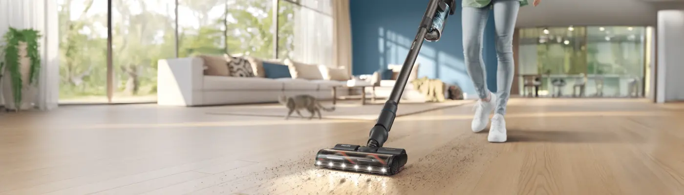 Person cleaning a hardwood floor with a Philips stick vacuum cleaner in a bright modern living room with a cat in the background Person cleaning a hardwood floor with a Philips stick vacuum cleaner in a bright modern living room with a cat in the background