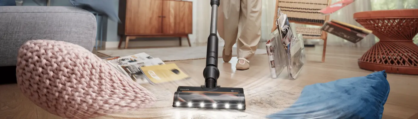 Philips PowerUp kabelloser Staubsauger reinigt den Boden eines modernen Wohnzimmers und saugt dabei Staub und Schmutz rund um Kissen und Haushaltsgegenstände auf. Philips PowerUp kabelloser Staubsauger reinigt den Boden eines modernen Wohnzimmers und saugt dabei Staub und Schmutz rund um Kissen und Haushaltsgegenstände auf.