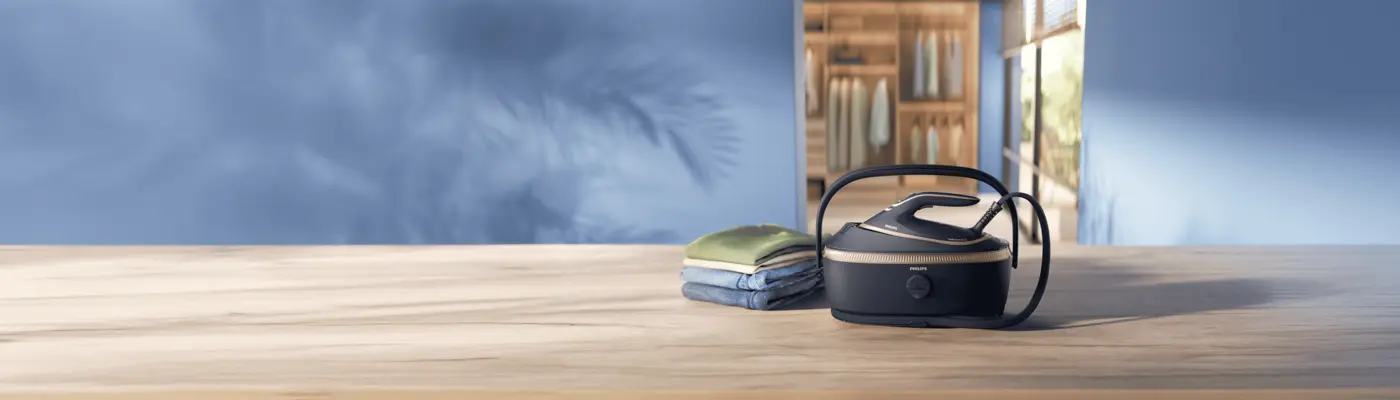 Stație de călcat cu generator de abur Philips pe o masă din lemn, lângă haine împăturite. Fundalul albastru și zona de dressing creează un decor modern și luminos, evidențiind produsul. Stație de călcat cu generator de abur Philips pe o masă din lemn, lângă haine împăturite. Fundalul albastru și zona de dressing creează un decor modern și luminos, evidențiind produsul.