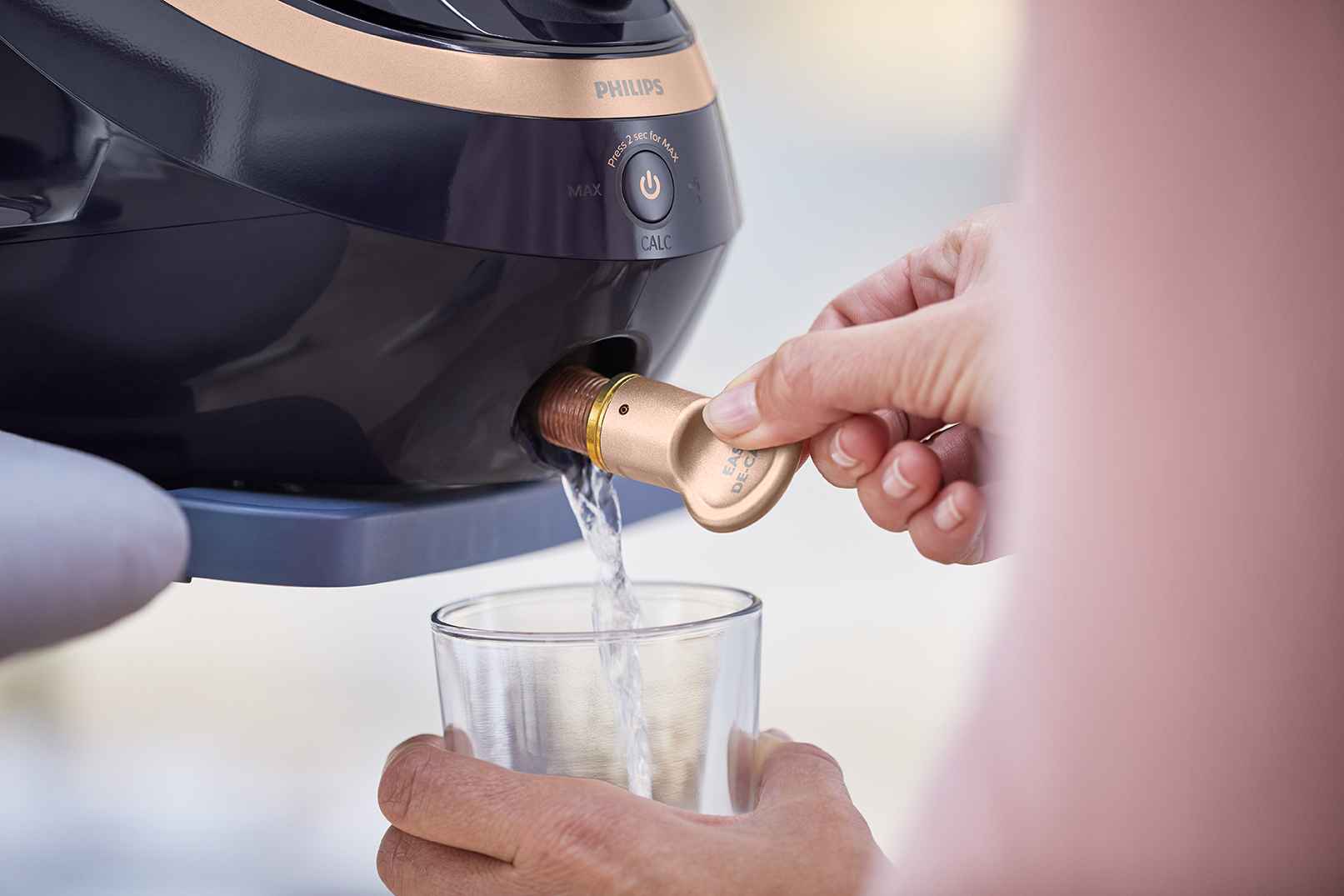 Nærbillede af en Philips Garment Care steamer's Easy De-Calc funktion i aktion. Vand drænes i et glas og viser den simple afkalkningsproces, der forlænger steamerens levetid. Nærbillede af en Philips Garment Care steamer's Easy De-Calc funktion i aktion. Vand drænes i et glas og viser den simple afkalkningsproces, der forlænger steamerens levetid.