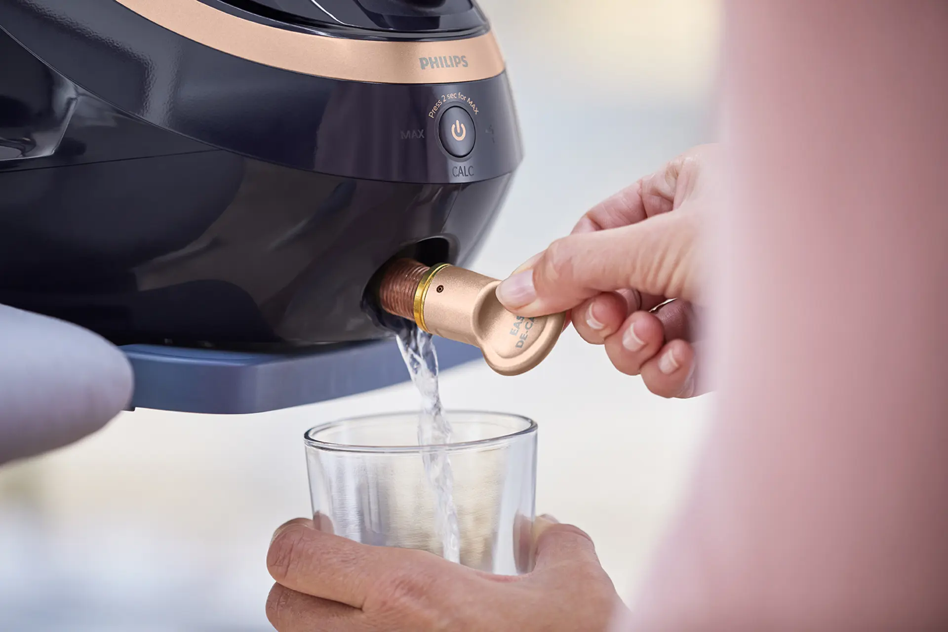 Zbliżenie na działanie funkcji Easy De-Calc parownicy do ubrań Philips Garment Care. Woda spływa do szklanki, pokazując prosty proces odkamieniania, który przedłuża żywotność parownicy. Zbliżenie na działanie funkcji Easy De-Calc parownicy do ubrań Philips Garment Care. Woda spływa do szklanki, pokazując prosty proces odkamieniania, który przedłuża żywotność parownicy.