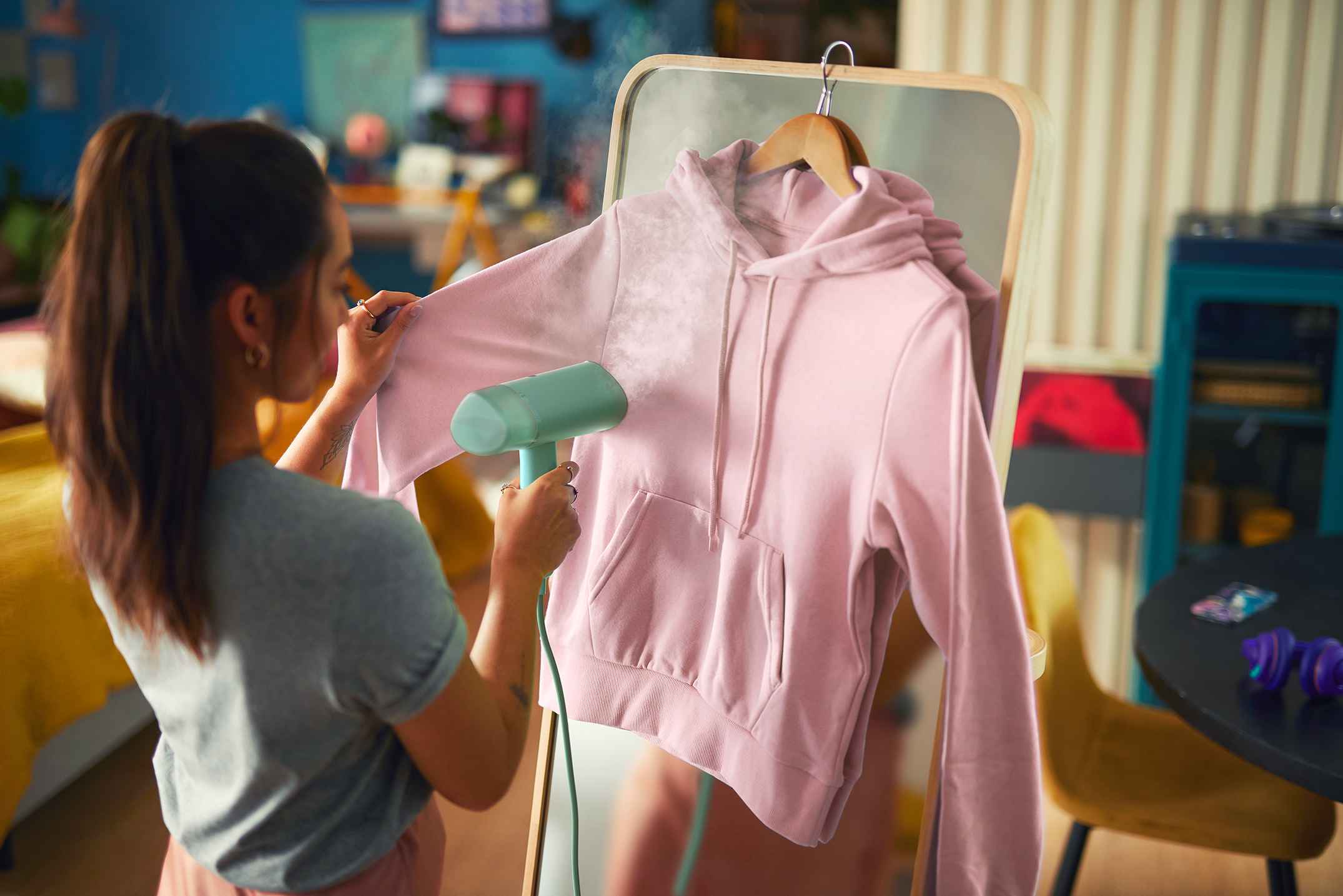 Eine Frau benutzt einen Philips Handdampfglätter, um einen hellrosa Hoodie aufzufrischen. Leicht und effektiv, ideal für die schnelle Faltenentfernung. Eine Frau benutzt einen Philips Handdampfglätter, um einen hellrosa Hoodie aufzufrischen. Leicht und effektiv, ideal für die schnelle Faltenentfernung.