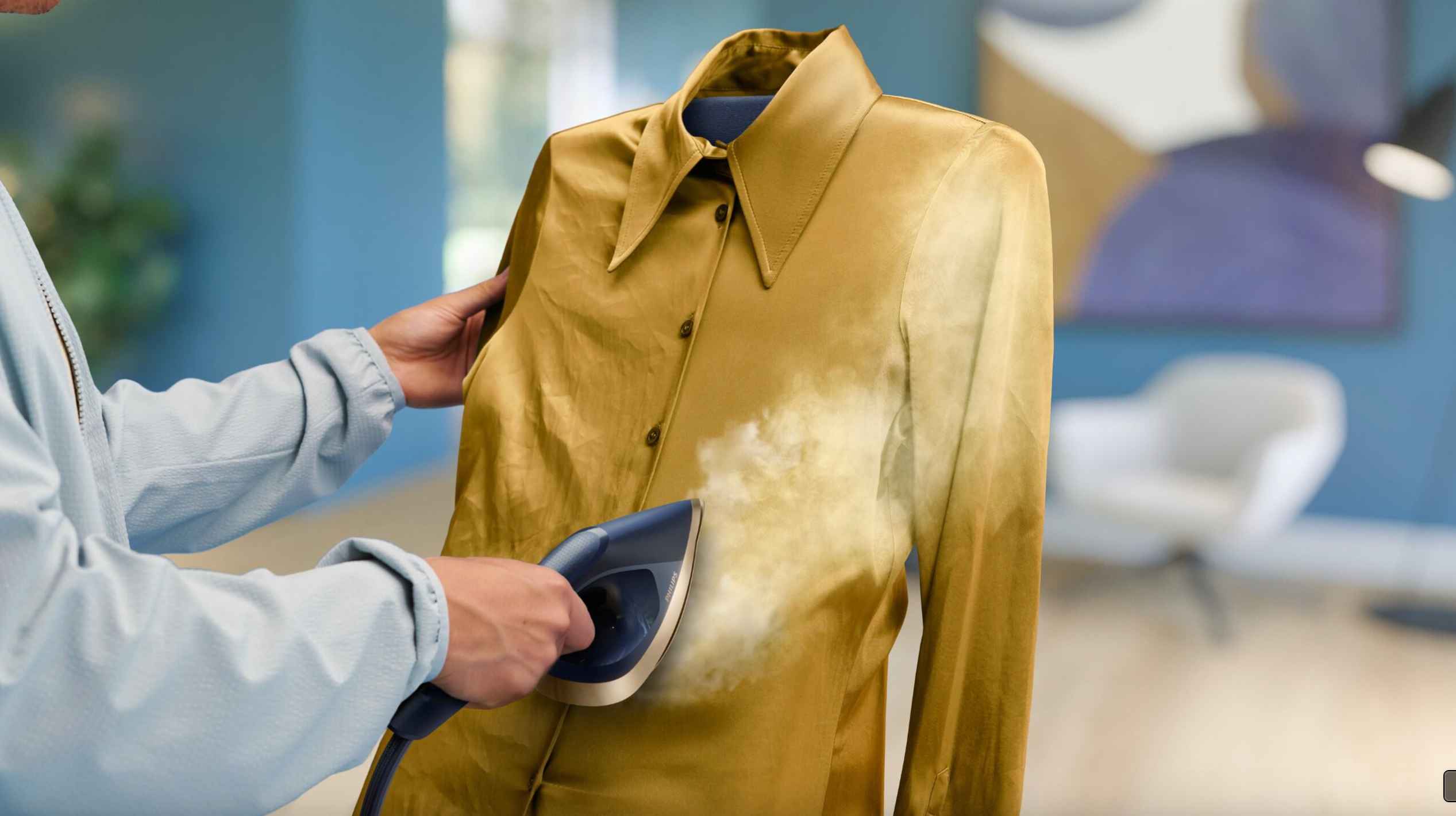 Philips Garment Care Steamer fjerner synlig rynker fra en gullfarget skjorte med krage. En rask og effektiv løsning for glatte, rynkefrie klær. Philips Garment Care Steamer fjerner synlig rynker fra en gullfarget skjorte med krage. En rask og effektiv løsning for glatte, rynkefrie klær.