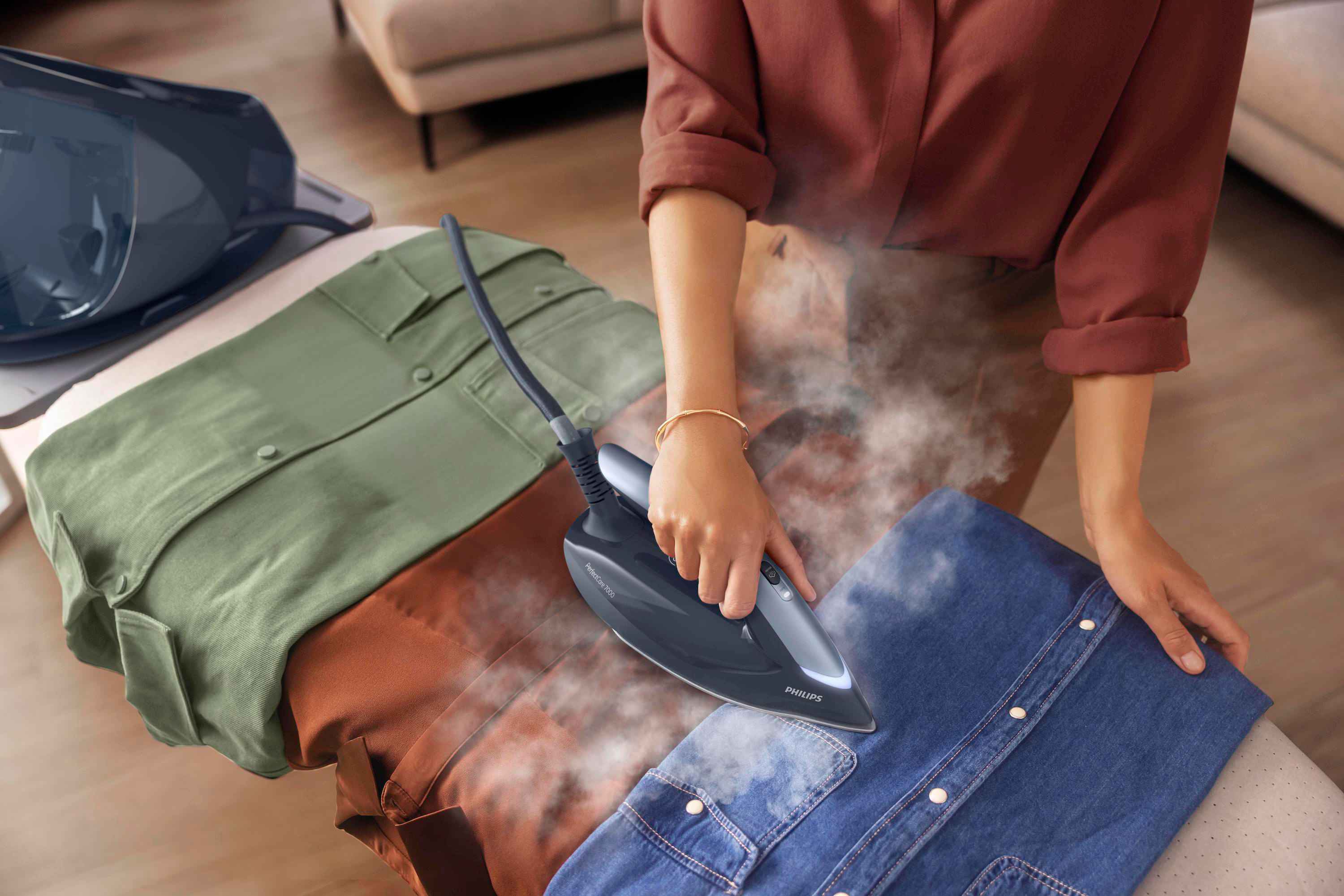 Philips klespleie: Kvinne damper en denimskjorte med PerfectCare 7000, og fremhever produktets elegante design. Synlig damp sikrer rask fjerning av rynker. Philips klespleie: Kvinne damper en denimskjorte med PerfectCare 7000, og fremhever produktets elegante design. Synlig damp sikrer rask fjerning av rynker.