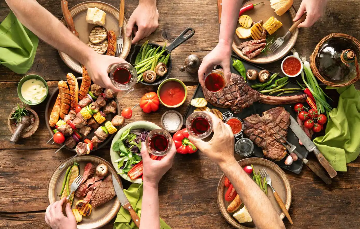 Overheadshot van een houten tafel vol gegrild vlees en bijgerechten, handen die proosten met wijn. Philips Grills & toasters leveren perfect gegrilde lekkernijen om te delen. Overheadshot van een houten tafel vol gegrild vlees en bijgerechten, handen die proosten met wijn. Philips Grills & toasters leveren perfect gegrilde lekkernijen om te delen.