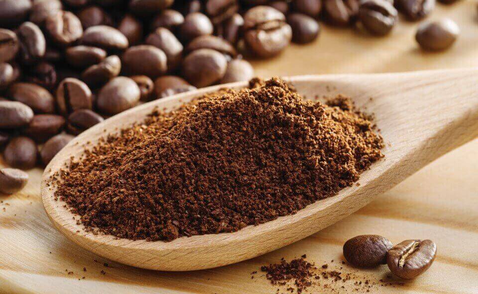 Zmielone ziarna kawy na łyżce, z całymi ziarnami kawy w tle Zmielone ziarna kawy na łyżce, z całymi ziarnami kawy w tle