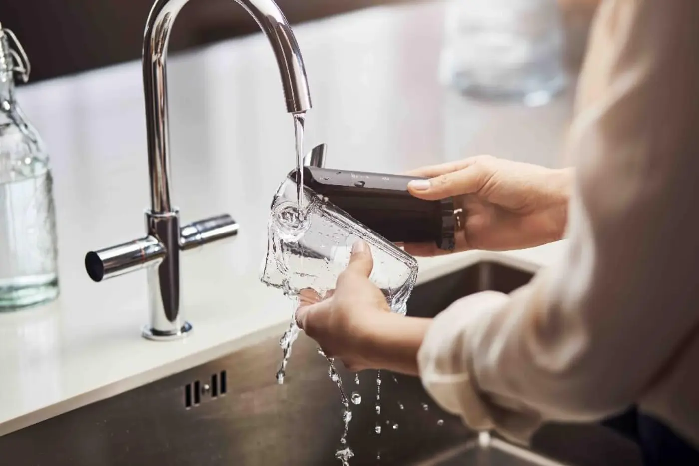 Osoba myje część ekspresu do kawy w zlewie kuchennym, używając wody płynącej z kranu. Osoba myje część ekspresu do kawy w zlewie kuchennym, używając wody płynącej z kranu.
