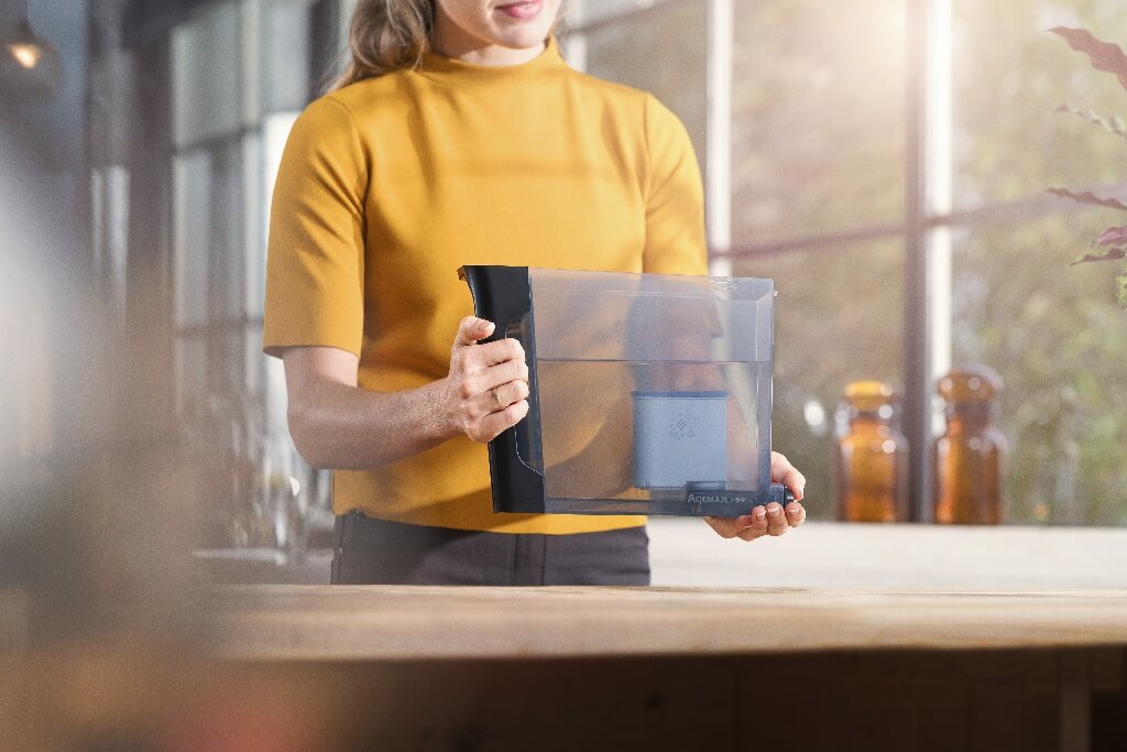 Kobieta stoi przy blacie kuchennym, trzymając część od ekspresu do kawy. Kobieta stoi przy blacie kuchennym, trzymając część od ekspresu do kawy.