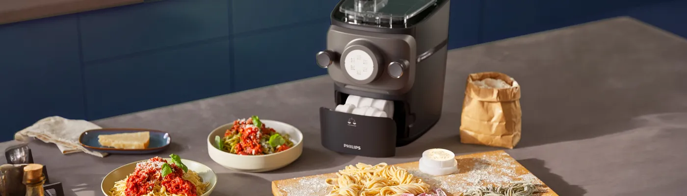 Philips-pastamachine met vers gemaakte, zelfgemaakte pasta op een met bloem bestrooide houten plank Philips-pastamachine met vers gemaakte, zelfgemaakte pasta op een met bloem bestrooide houten plank