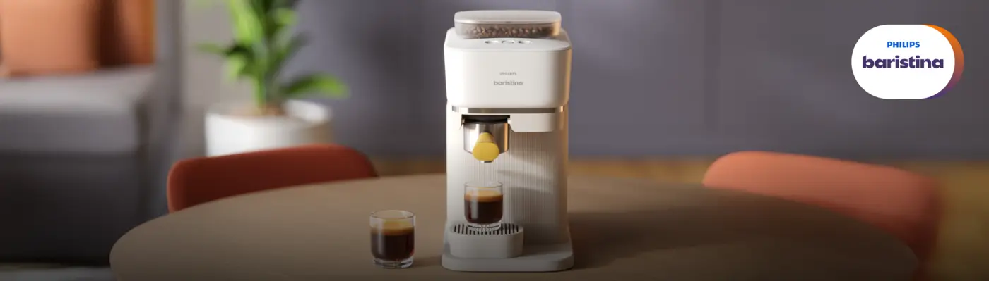 Machine à café Philips Baristina sur une table en bois dans un intérieur moderne, préparant un espresso dans un verre. Un second espresso est posé à côté, tandis qu’une plante floue et des chaises créent une ambiance chaleureuse. Machine à café Philips Baristina sur une table en bois dans un intérieur moderne, préparant un espresso dans un verre. Un second espresso est posé à côté, tandis qu’une plante floue et des chaises créent une ambiance chaleureuse.