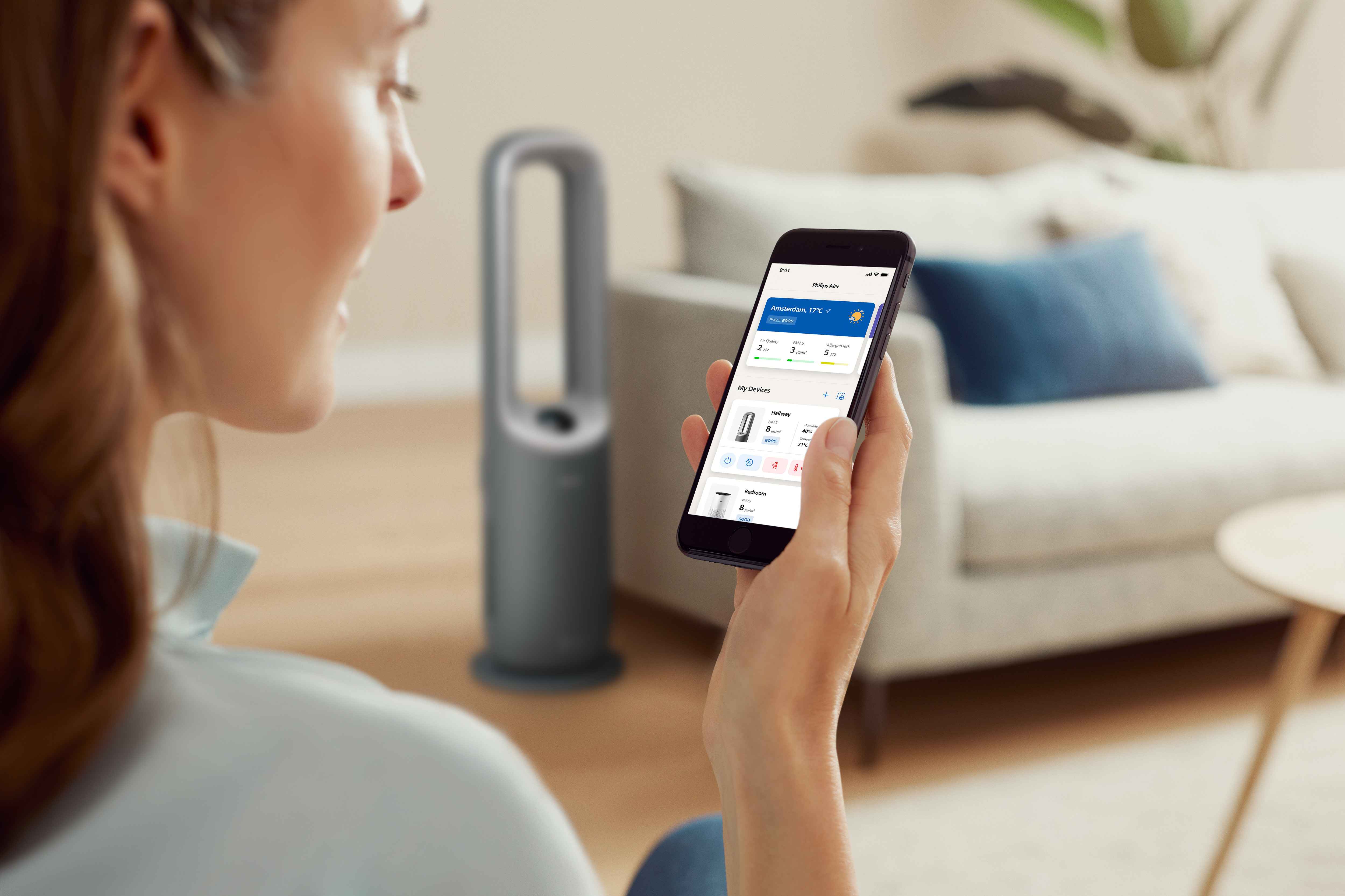 Kvinne bruker Philips multifunksjonell luftrenser via app. Viser luftkvalitetsdata i sanntid. Strømlinjeformet design i lys stue, for optimal klimakontroll. Kvinne bruker Philips multifunksjonell luftrenser via app. Viser luftkvalitetsdata i sanntid. Strømlinjeformet design i lys stue, for optimal klimakontroll.