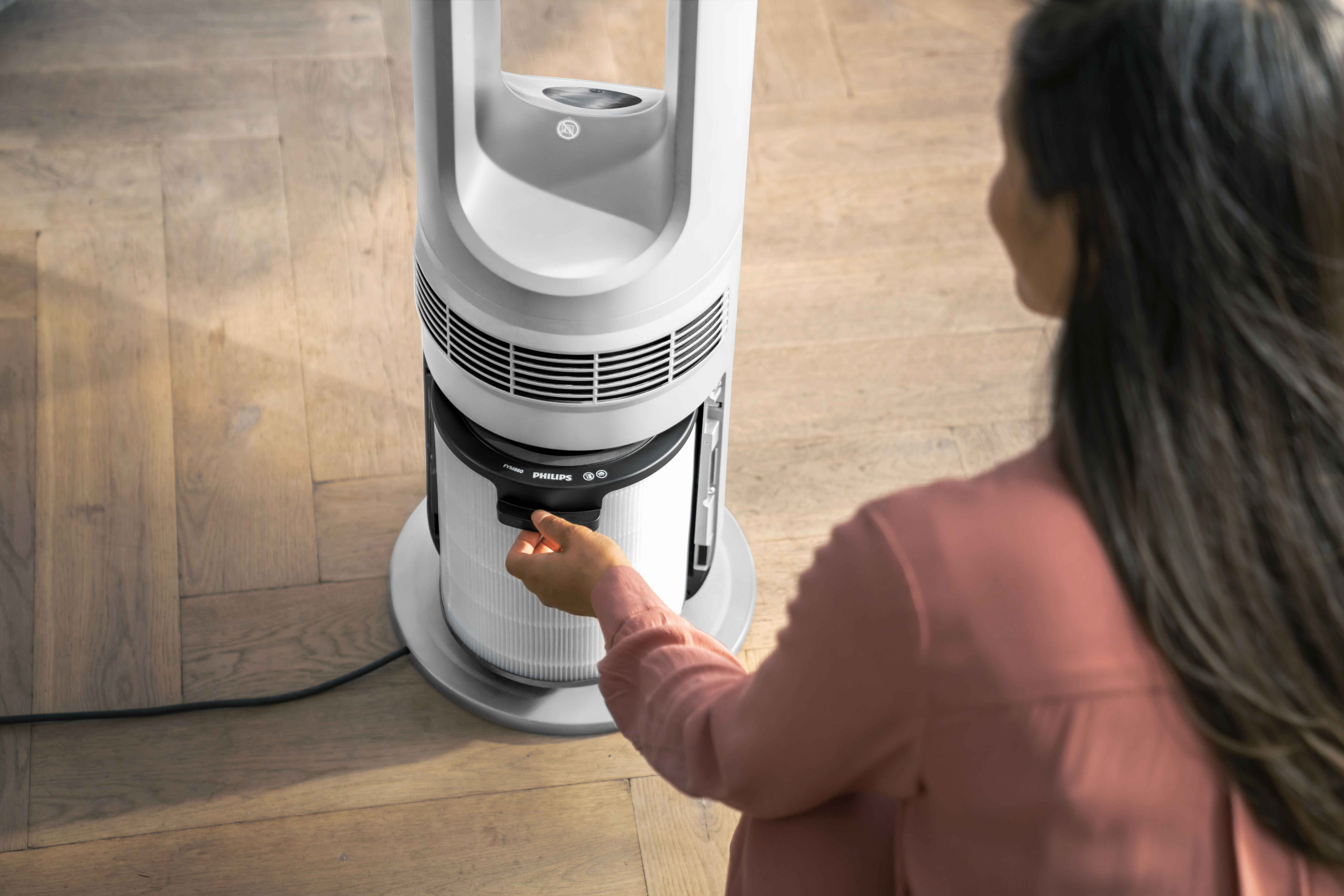 Osoba uzyskująca dostęp do filtra w eleganckim, białym wentylatorze wieżowym Philips Multifunctional Climate Care, dla optymalnego zarządzania klimatem w domu. Osoba uzyskująca dostęp do filtra w eleganckim, białym wentylatorze wieżowym Philips Multifunctional Climate Care, dla optymalnego zarządzania klimatem w domu.