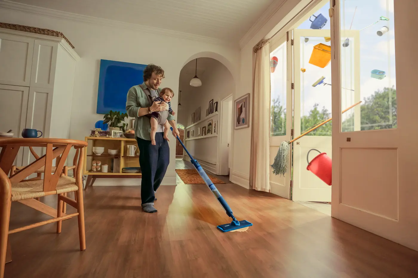 Ojciec wykonujący wiele zadań jednocześnie, mopując podłogę za pomocą OneUp, trzymając uśmiechnięte dziecko w jasnym, nowoczesnym domu, z unoszącymi się środkami czystości za otwartymi drzwiami. Ojciec wykonujący wiele zadań jednocześnie, mopując podłogę za pomocą OneUp, trzymając uśmiechnięte dziecko w jasnym, nowoczesnym domu, z unoszącymi się środkami czystości za otwartymi drzwiami.