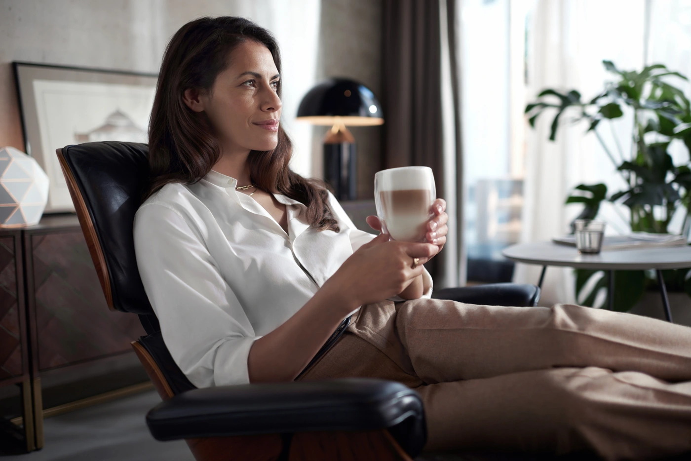 Kobieta relaksuje się, trzymając warstwową kawę z Philips Saeco Xelsis. Przekazuje osobisty luksus i doznanie kawy premium. Kobieta relaksuje się, trzymając warstwową kawę z Philips Saeco Xelsis. Przekazuje osobisty luksus i doznanie kawy premium.