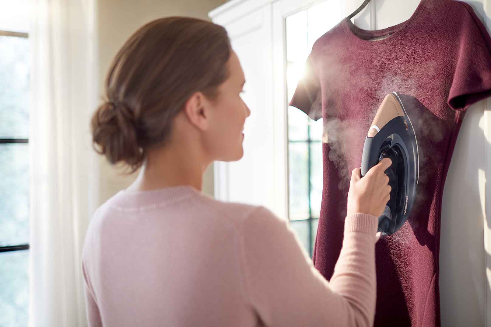 Frau, die einen Philips Steam Generators PerfectCare 9000 verwendet, um ein kastanienbraunes Kleid zu dämpfen. Überlegenes Design bietet ein unvergleichliches Benutzererlebnis. Bügeln neu erfunden. Frau, die einen Philips Steam Generators PerfectCare 9000 verwendet, um ein kastanienbraunes Kleid zu dämpfen. Überlegenes Design bietet ein unvergleichliches Benutzererlebnis. Bügeln neu erfunden.