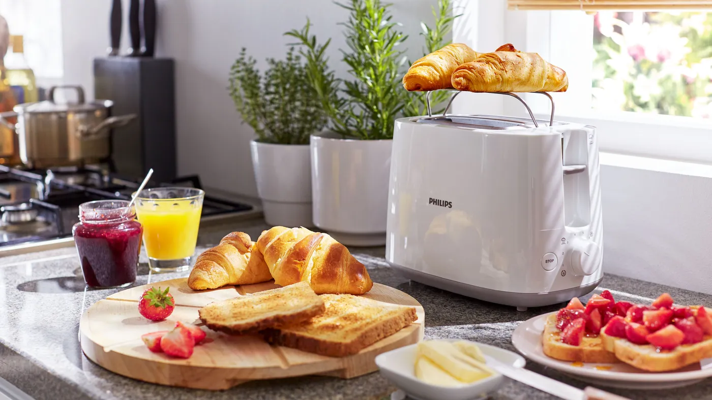 Biały toster Philips z rusztem do podgrzewania i croissantami na nowoczesnym blacie kuchennym z tostami i dodatkami śniadaniowymi Biały toster Philips z rusztem do podgrzewania i croissantami na nowoczesnym blacie kuchennym z tostami i dodatkami śniadaniowymi