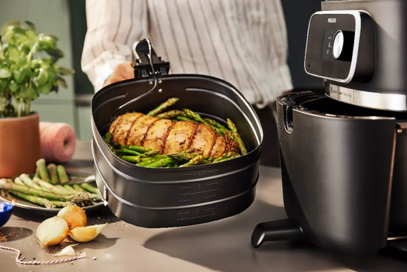 Osoba trzyma kosz ze smażonym mięsem obok frytkownicy marki Philips. Osoba trzyma kosz ze smażonym mięsem obok frytkownicy marki Philips.