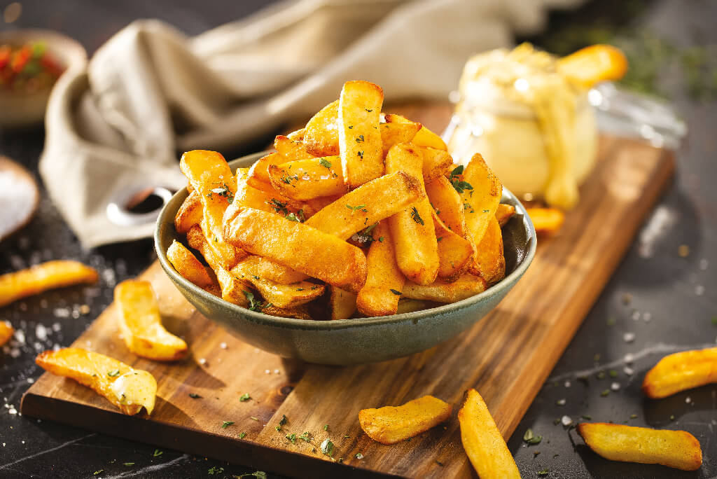 Frytki z airfryera w misce umieszczonej na drewnianej desce do krojenia. Frytki z airfryera w misce umieszczonej na drewnianej desce do krojenia.