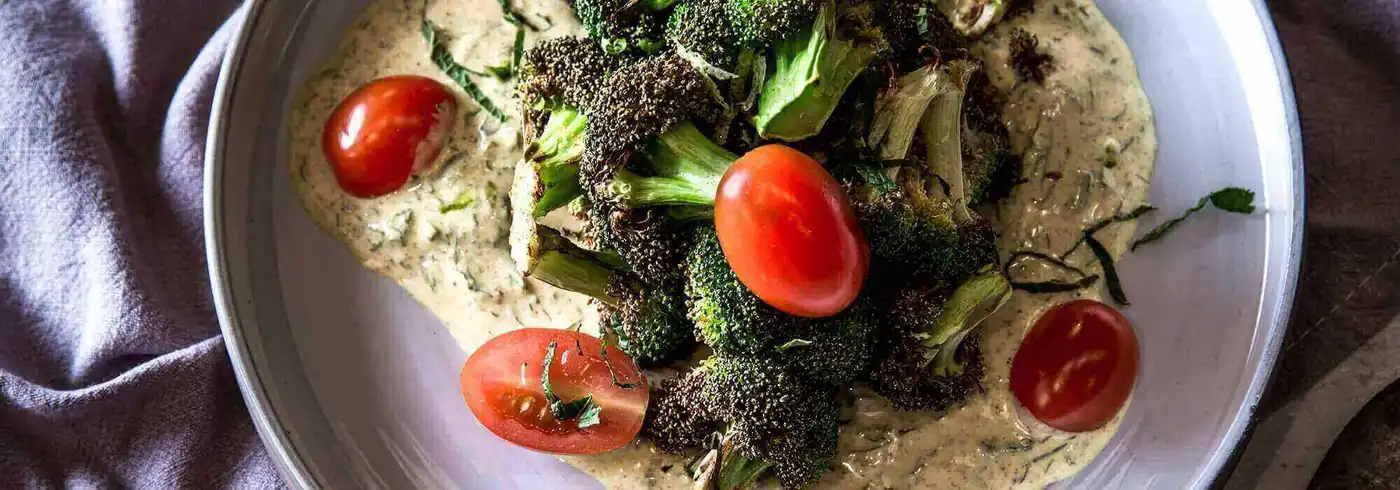 A plate featuring air-fried broccoli and tomatoes, served with a side of curry yogurt A plate featuring air-fried broccoli and tomatoes, served with a side of curry yogurt