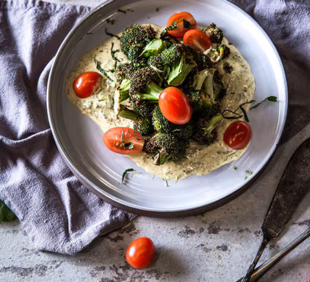 A dish of air-fried broccoli and tomatoes accompanied by curry yogurt on a white plate A dish of air-fried broccoli and tomatoes accompanied by curry yogurt on a white plate