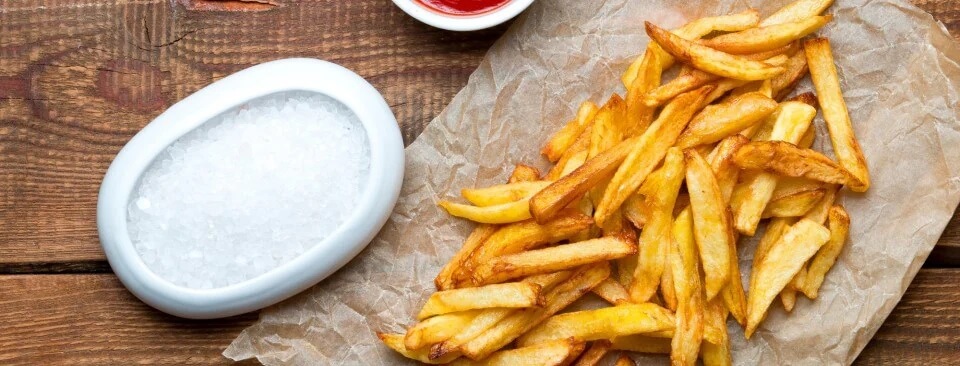 Porcja chrupiących frytek z air fryera na drewnianym blacie, obok biały pojemnik z solą Porcja chrupiących frytek z air fryera na drewnianym blacie, obok biały pojemnik z solą