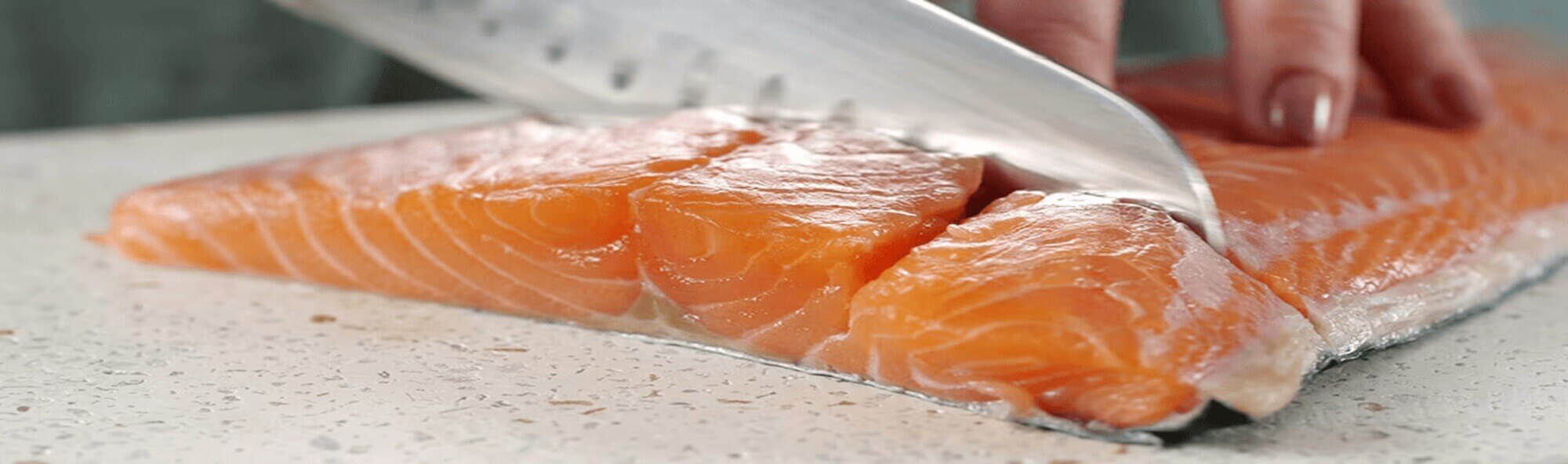 Närbild på färsk laxfilé som skivas med en kniv på en vitspräcklig skärbräda. Fiskens livfulla orange färg och marmorerade textur syns tydligt och framhäver dess färskhet. Närbild på färsk laxfilé som skivas med en kniv på en vitspräcklig skärbräda. Fiskens livfulla orange färg och marmorerade textur syns tydligt och framhäver dess färskhet.