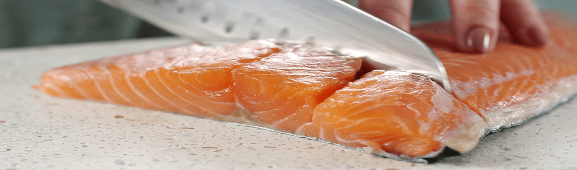 Et nærbillede af en frisk laksefilet, der skæres med en kniv på en hvid plettet skærebræt. Den livlige orange farve og marmorerede tekstur af fisken er tydeligt synlige, hvilket fremhæver dens friskhed. Et nærbillede af en frisk laksefilet, der skæres med en kniv på en hvid plettet skærebræt. Den livlige orange farve og marmorerede tekstur af fisken er tydeligt synlige, hvilket fremhæver dens friskhed.