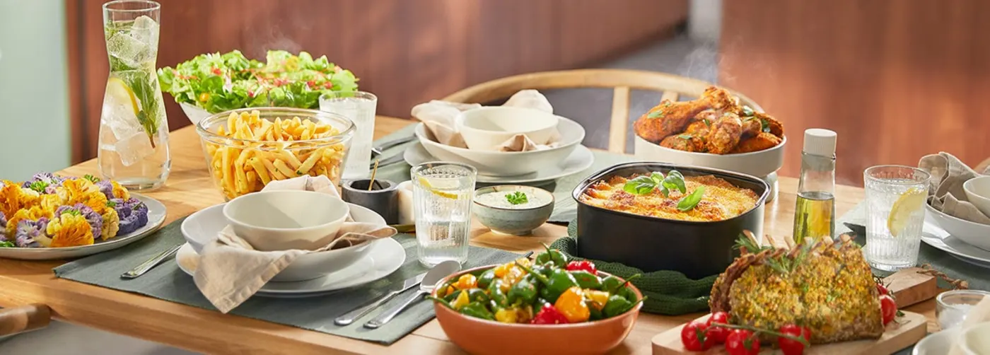 Et koselig spisebord fylt med ulike retter: fargerik blomkål, frisk salat, sprø pommes frites, bakt lasagne, krydrede kyllinglår, stekte grønnsaker, urtestekt stek og forfriskende drinker. Et koselig spisebord fylt med ulike retter: fargerik blomkål, frisk salat, sprø pommes frites, bakt lasagne, krydrede kyllinglår, stekte grønnsaker, urtestekt stek og forfriskende drinker.