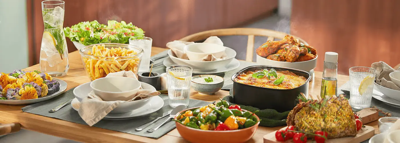 Et hyggeligt spisebord fyldt med forskellige retter: farverig blomkål, frisk salat, sprøde pomfritter, bagt lasagne, krydrede kyllingelår, ristede grøntsager, urteindbagt steg og forfriskende drikke. Et hyggeligt spisebord fyldt med forskellige retter: farverig blomkål, frisk salat, sprøde pomfritter, bagt lasagne, krydrede kyllingelår, ristede grøntsager, urteindbagt steg og forfriskende drikke.